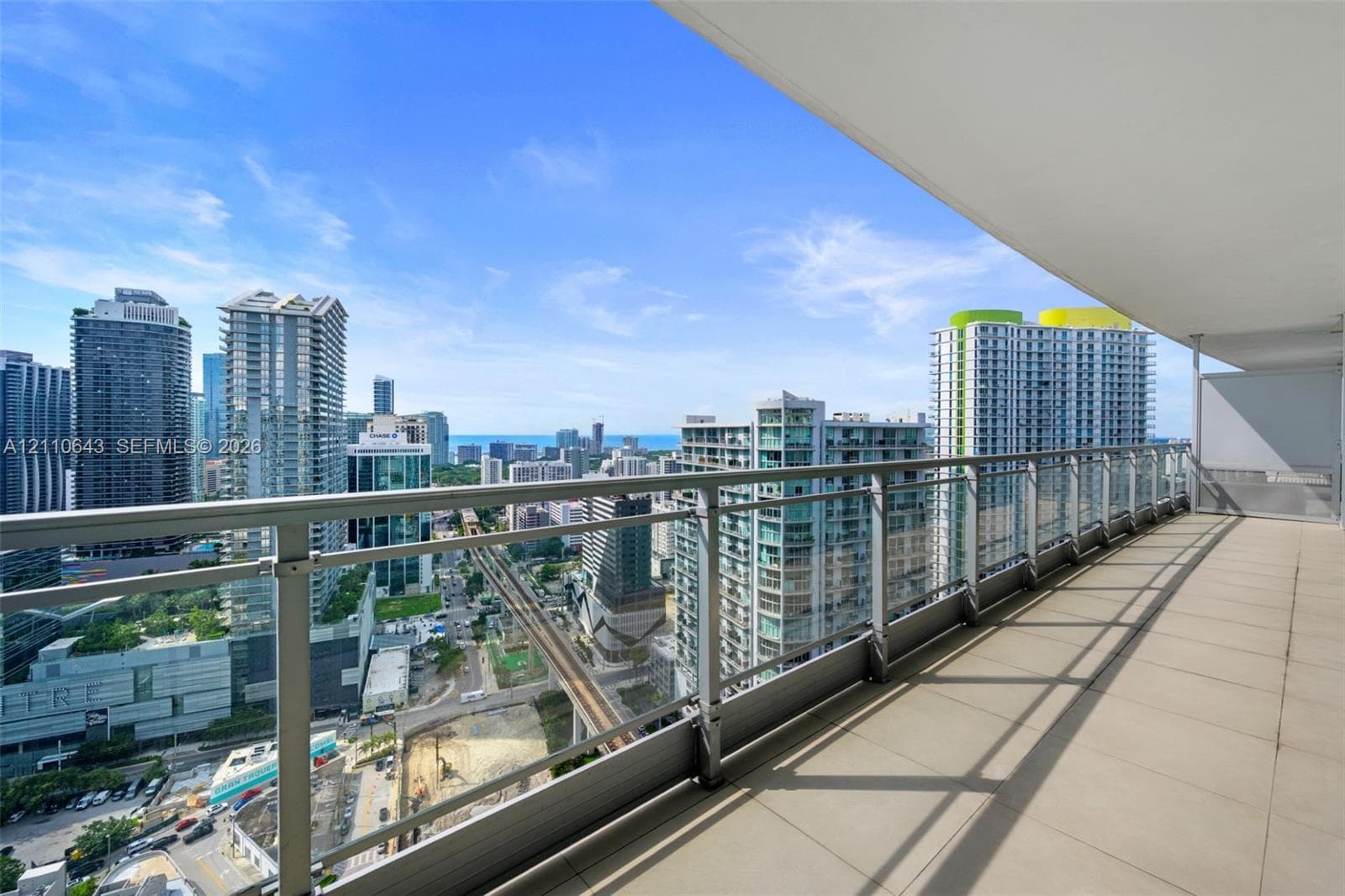 Covered balcony featuring neutral tile flooring and a glass railing with metal framing, offering a cityscape panorama