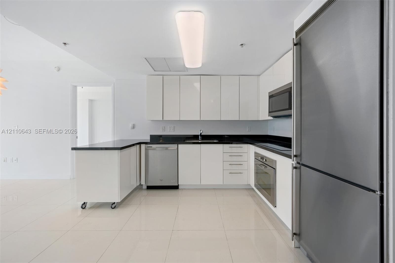 Kitchen featuring white flat-panel cabinetry, dark stone countertops, stainless steel appliances, and tile flooring