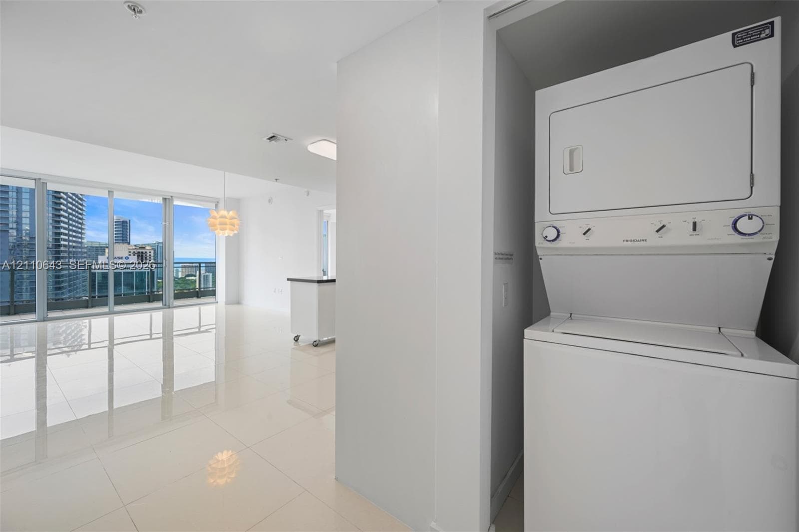 Stacked washer and dryer unit, floor-to-ceiling glass sliding doors, polished tile flooring, and ceiling-mounted lighting
