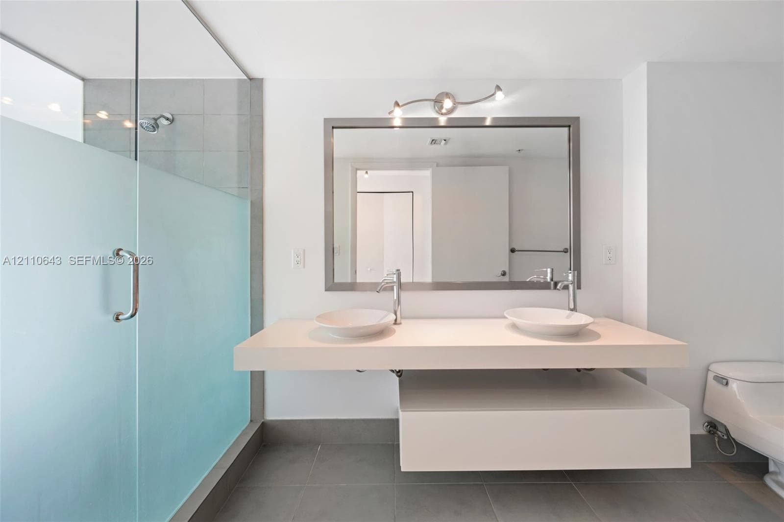 Floating double vanity with dual vessel sinks, quartz-finish countertop, matte metal fixtures, frosted glass shower enclosure, and large-format tile flooring