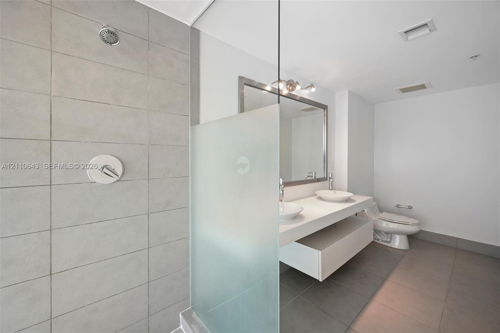Bathroom featuring a dual-sink floating vanity, a walk-in shower with large-format tile surround and a frosted glass panel, and polished chrome fixtures