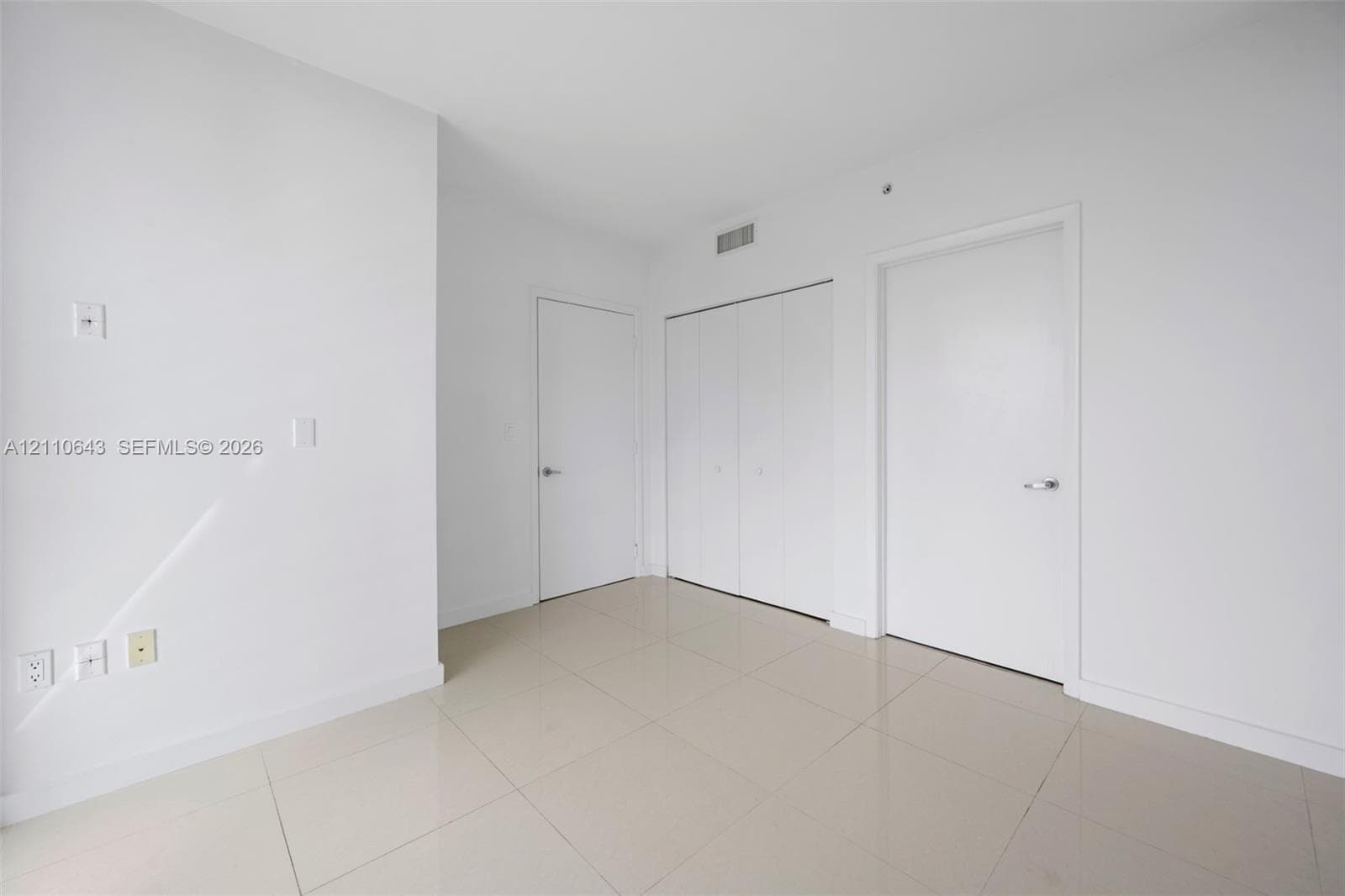 Neutral interior space featuring polished tile flooring, smooth wall finishes, two interior doors, and a double-door reach-in closet
