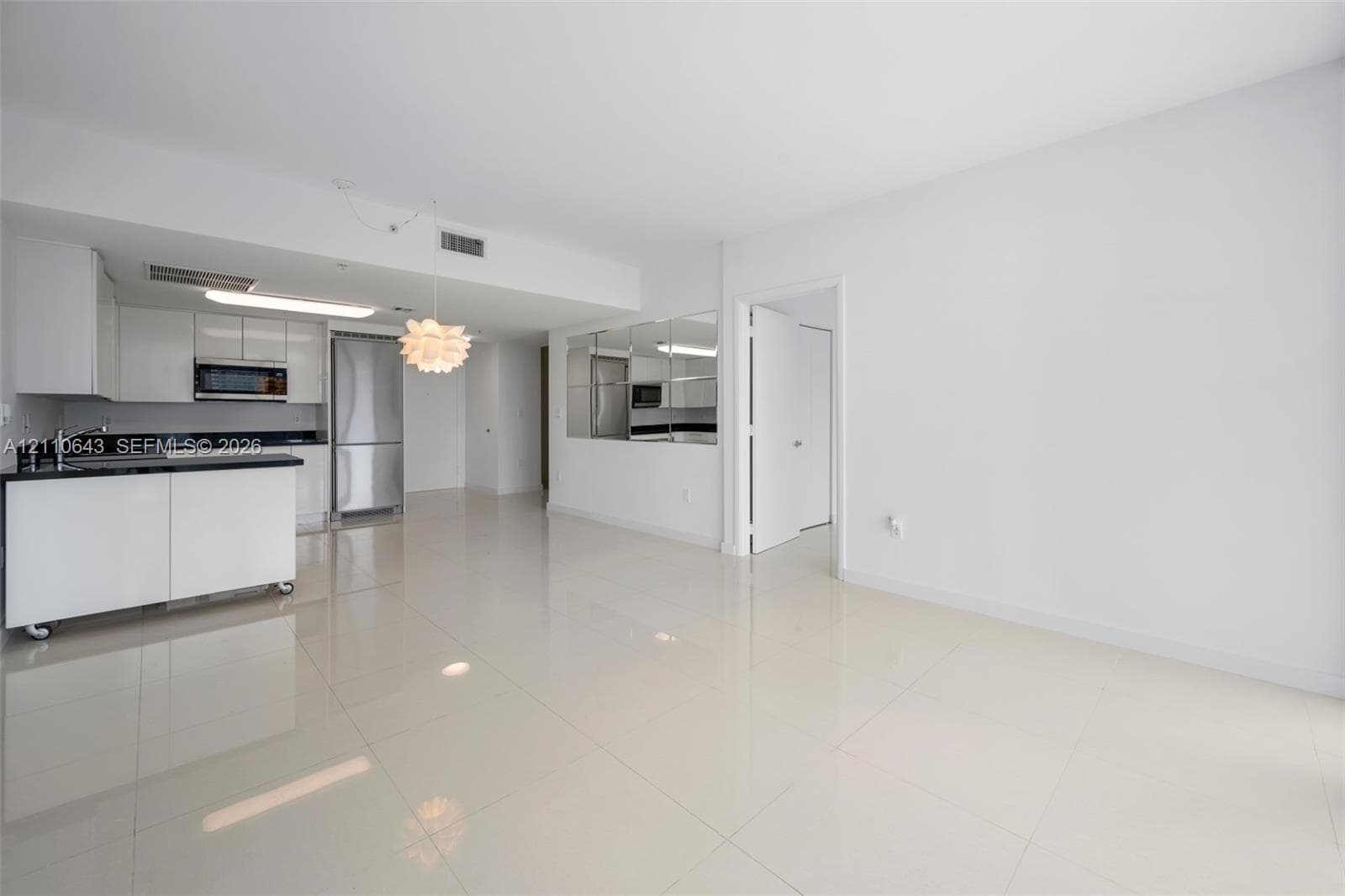 Open-concept kitchen featuring high-gloss cabinetry, dark stone countertops, stainless steel appliances, polished tile flooring, and a mirrored wall panel