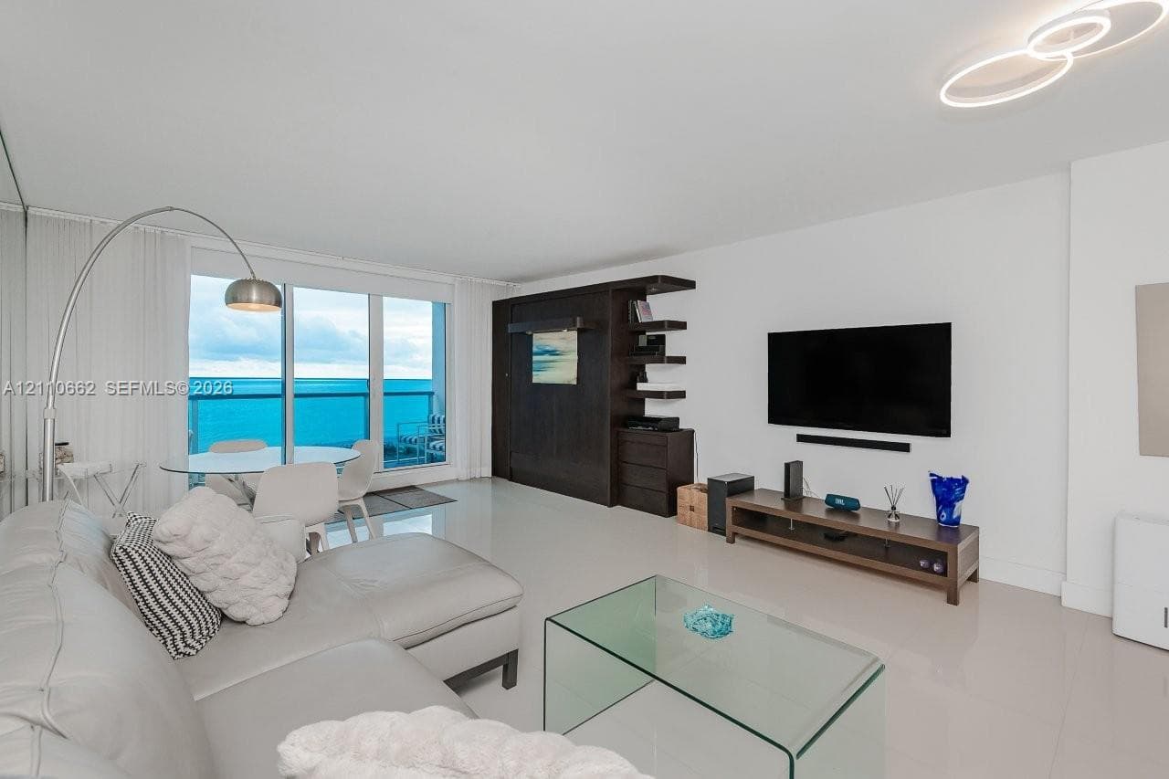 Open-concept living space featuring high-gloss tile flooring, floor-to-ceiling wall mirror, recessed lighting, and kitchen with breakfast bar and built-in cabinetry