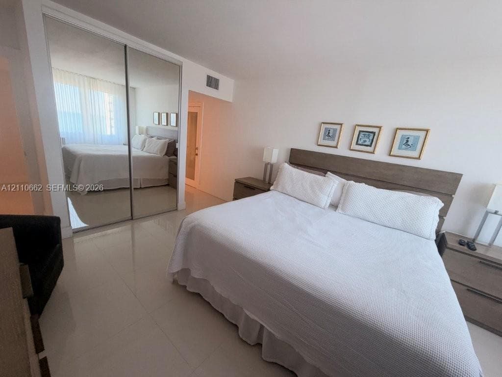 Bedroom featuring large-format light-toned tile flooring, floor-to-ceiling mirrored sliding closet doors, and smooth-finish walls
