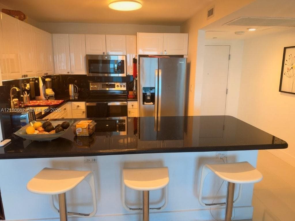Kitchen featuring white cabinetry, black stone countertops, stainless steel appliances, and a breakfast bar