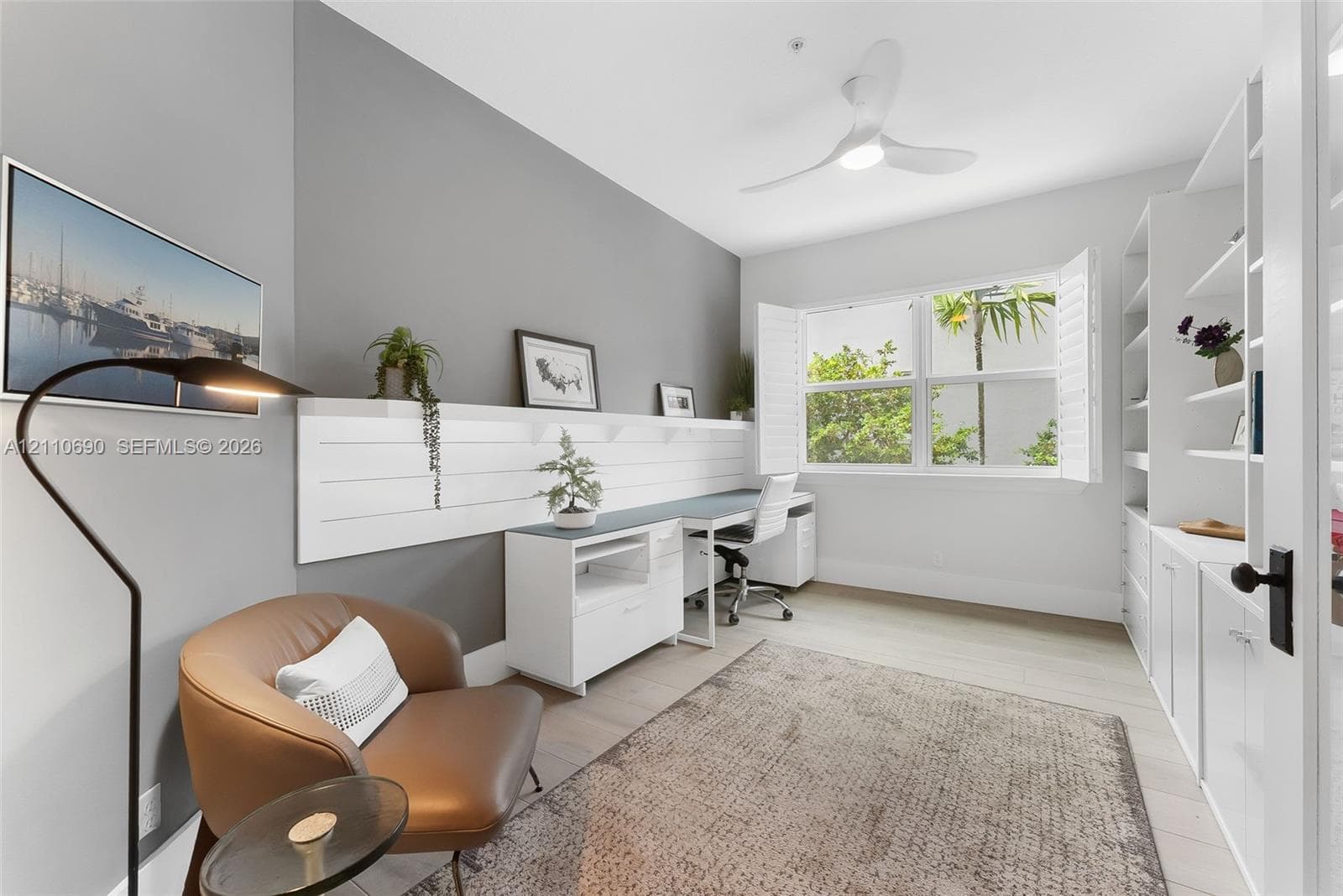Built-in white shelving, wood-finish flooring, white plantation shutters, three-blade ceiling fan with integrated light, and white shiplap accent wall