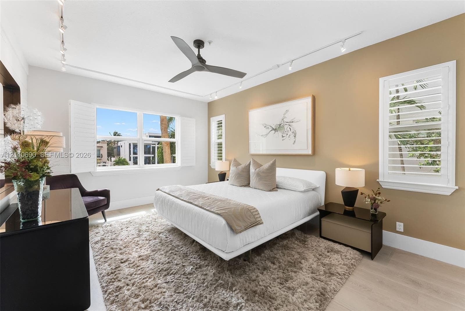 Bedroom featuring light wood-finish flooring, white plantation shutters, a contemporary ceiling fan, and adjustable track lighting
