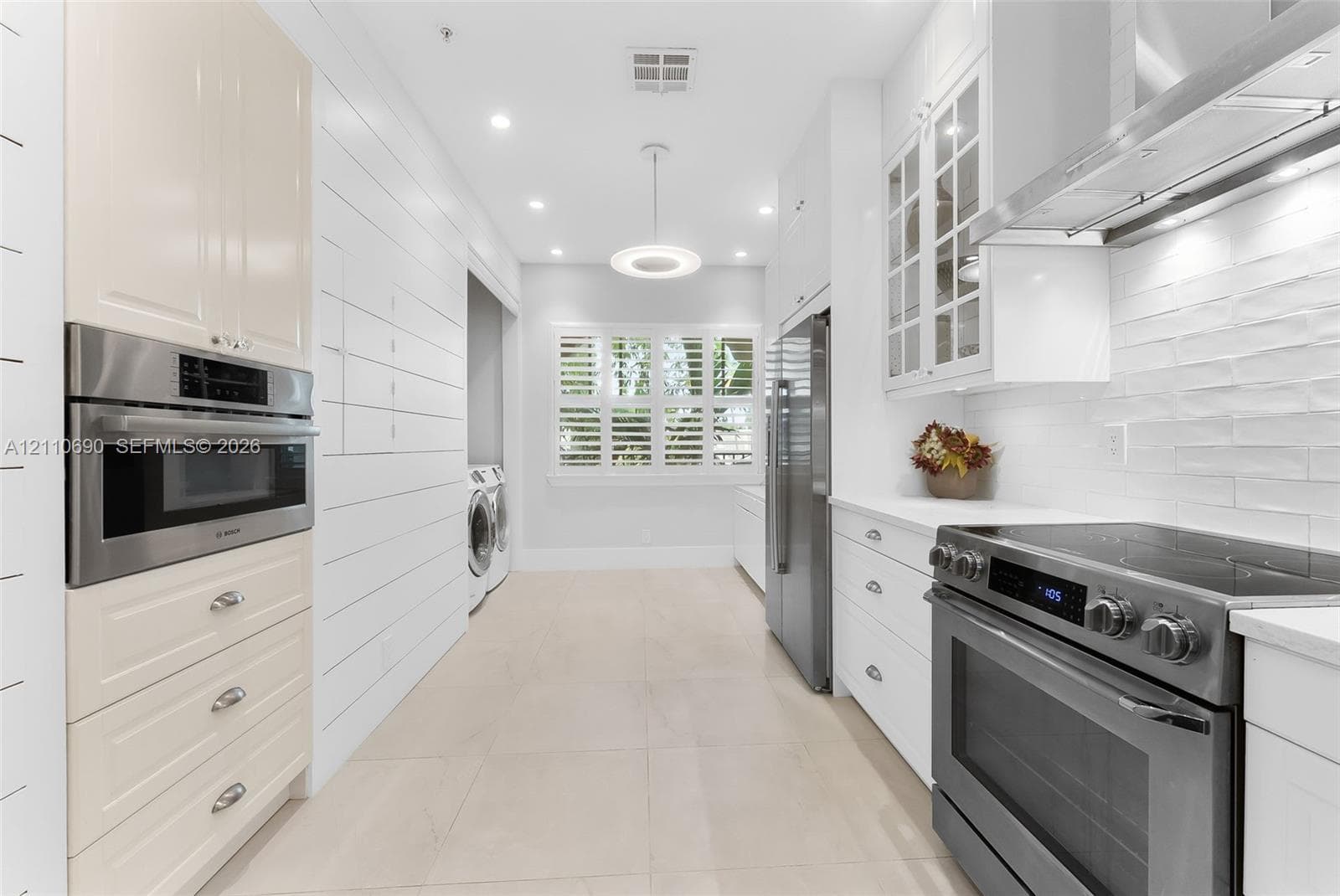 Kitchen featuring white Shaker-style cabinetry, stainless steel appliances, shiplap wall paneling, tile flooring, and interior window shutters