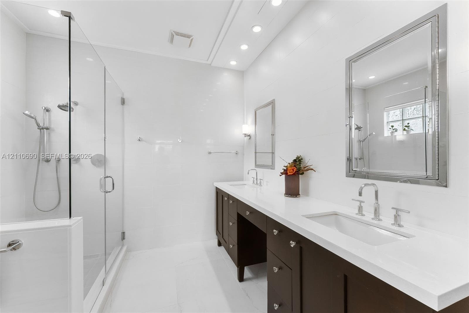Double vanity featuring dark cabinetry, solid-surface countertops, recessed lighting, and a glass-enclosed walk-in shower with a multi-function showerhead