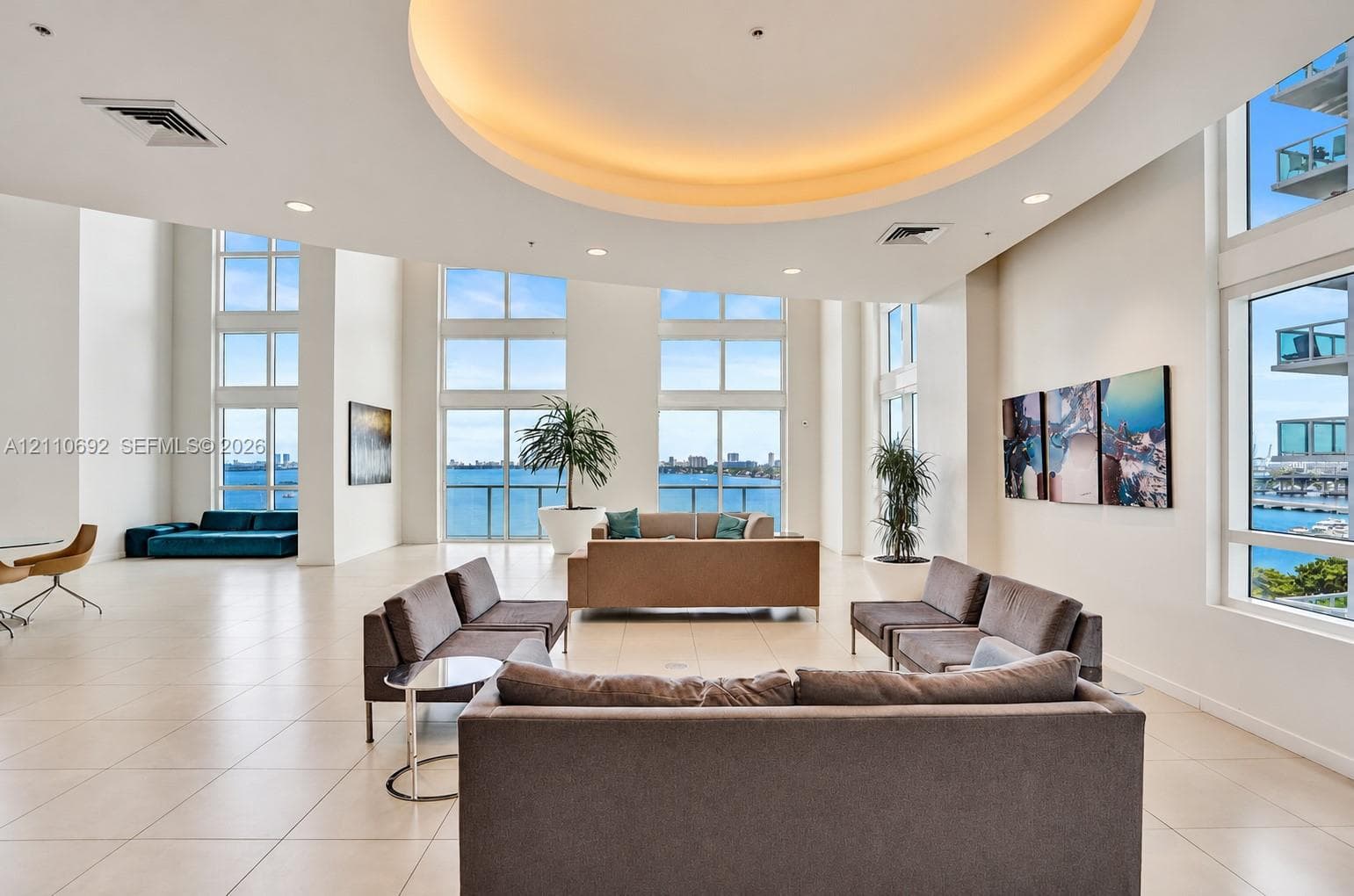 Expansive open-concept room featuring floor-to-ceiling windows, polished tile flooring, a recessed circular tray ceiling with integrated lighting, and multiple balconies