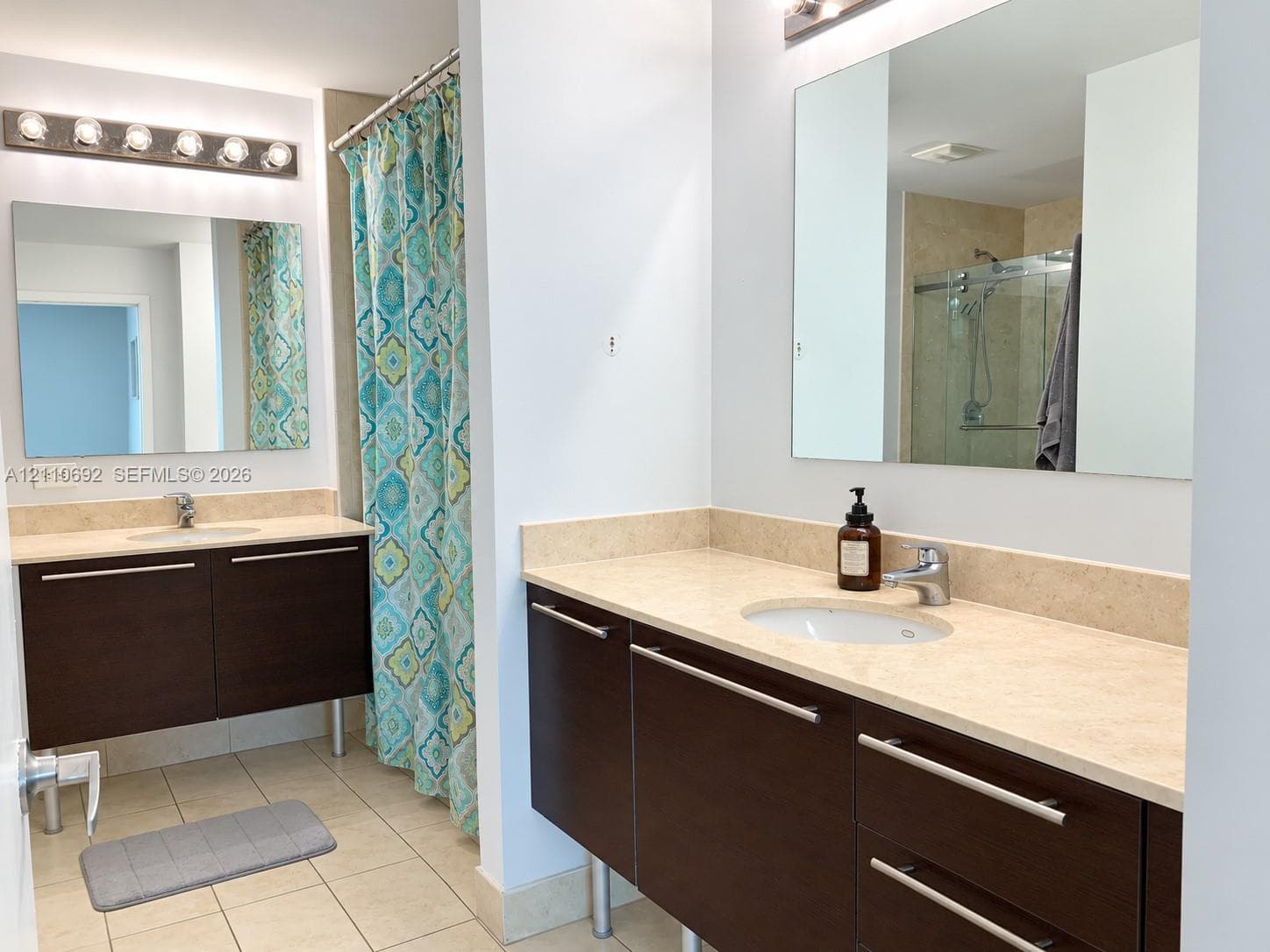 Dual floating vanities featuring dark wood-finish cabinetry, light-toned stone countertops, undermount sinks, and polished hardware, complemented by full-width vanity mirrors and tile flooring