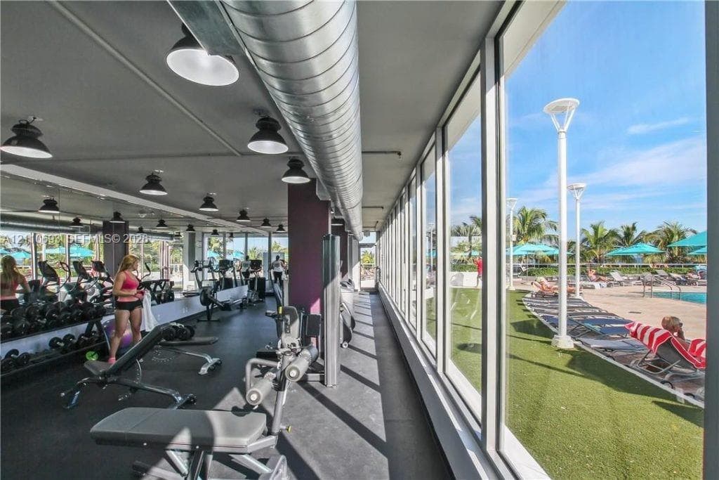 Fitness center featuring floor-to-ceiling windows, industrial exposed ductwork, recessed pendant lighting, and rubberized flooring