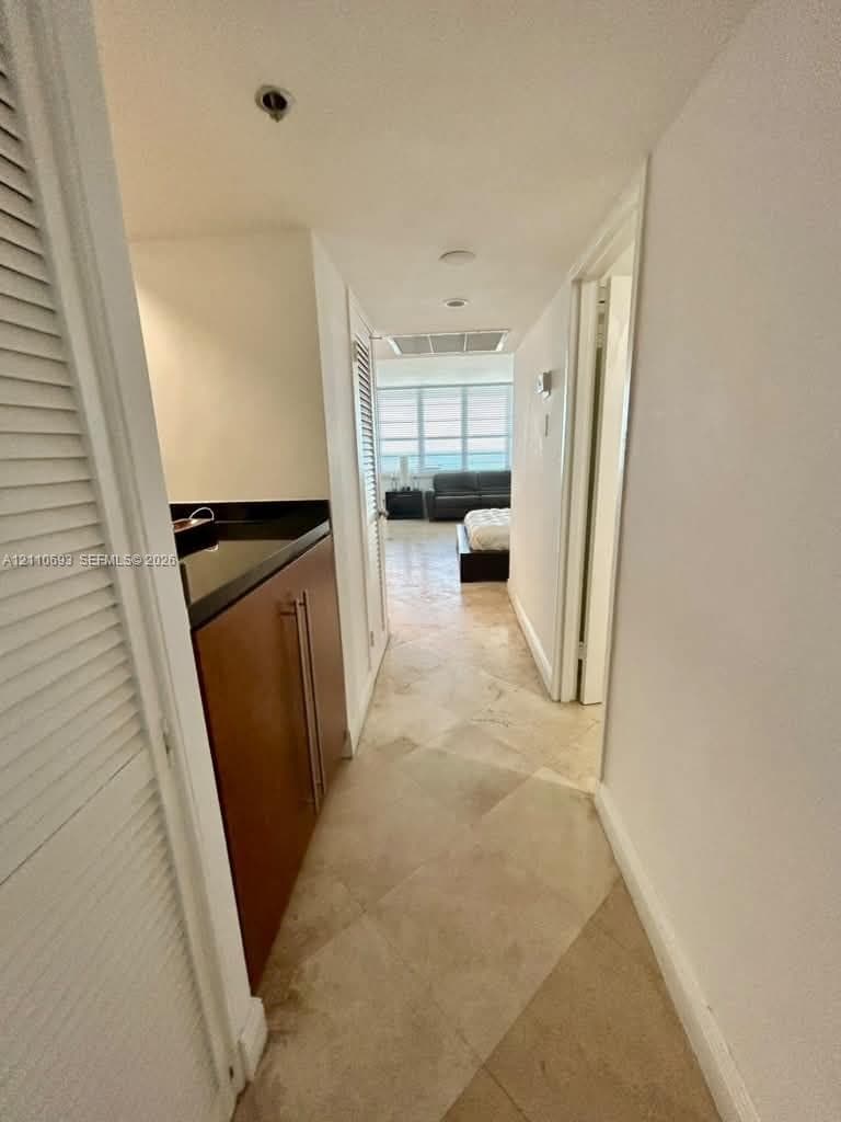 Hallway featuring polished stone tile flooring, built-in cabinetry with a dark stone countertop, and louvered closet doors