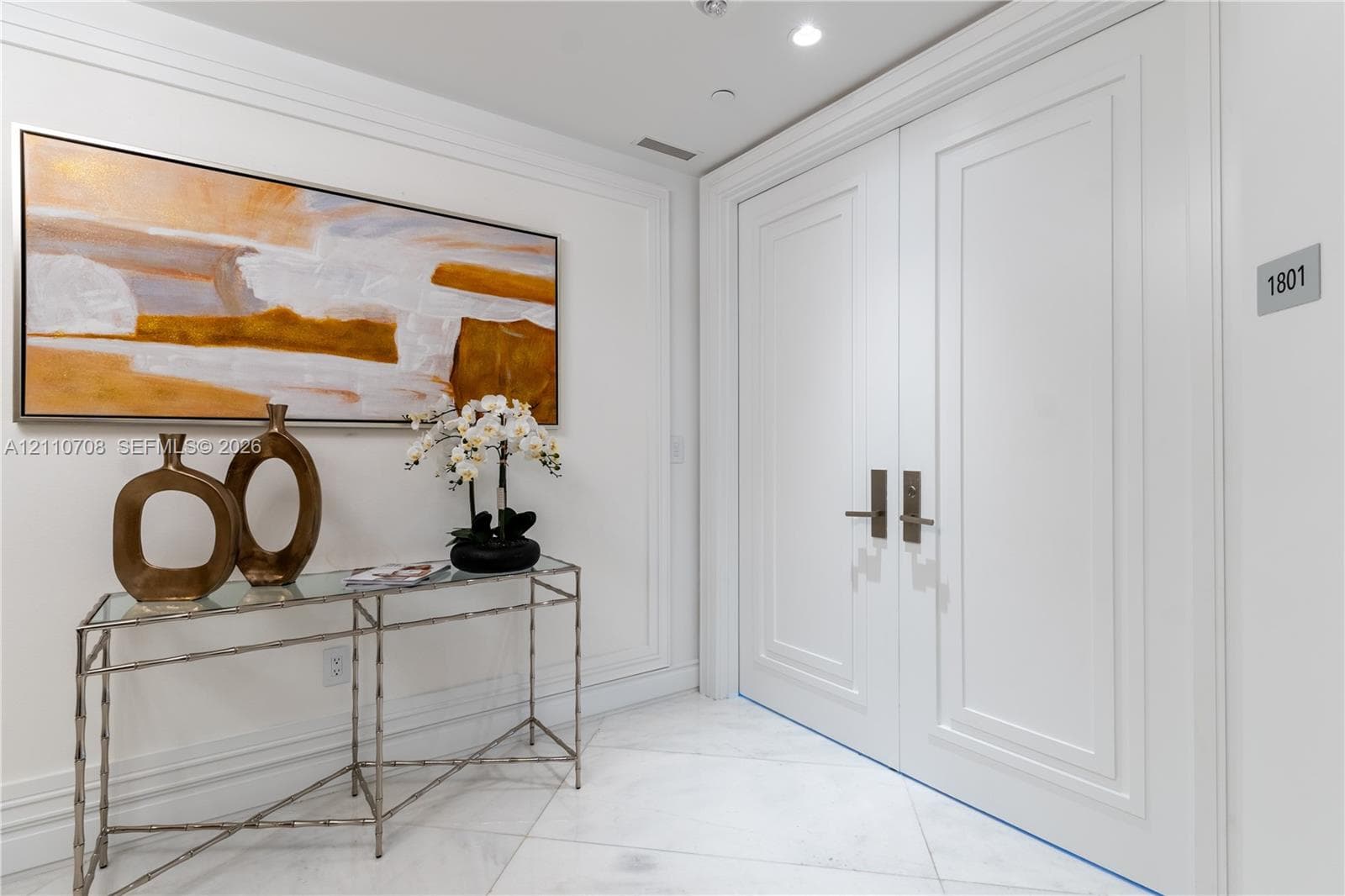 Expansive lobby featuring high ceilings with recessed lighting, tiered crystal chandeliers, textured wall finishes, and a structural column with decorative stone detailing