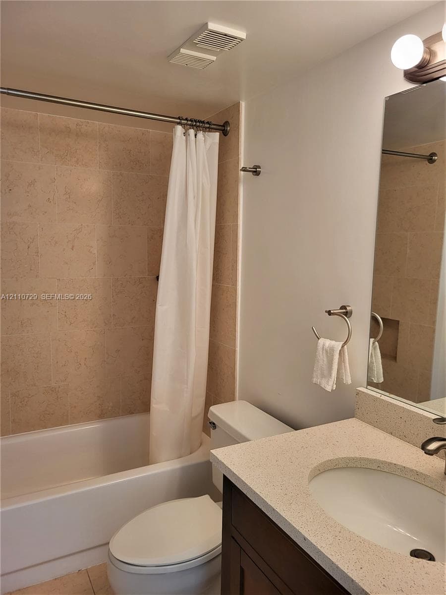 Bathroom featuring a shower-tub combination with stone-tile surround, vanity with solid-surface countertop, integrated basin, and wall-mounted vanity lighting