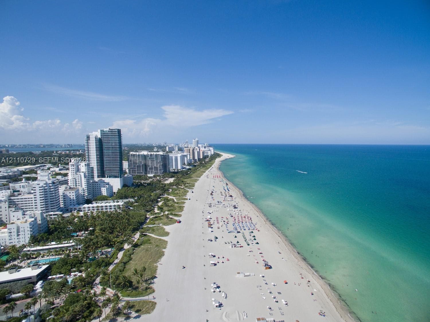 Aerial perspective of coastal landscape featuring a wide sandy beach, turquoise ocean waters, and a dense urban skyline