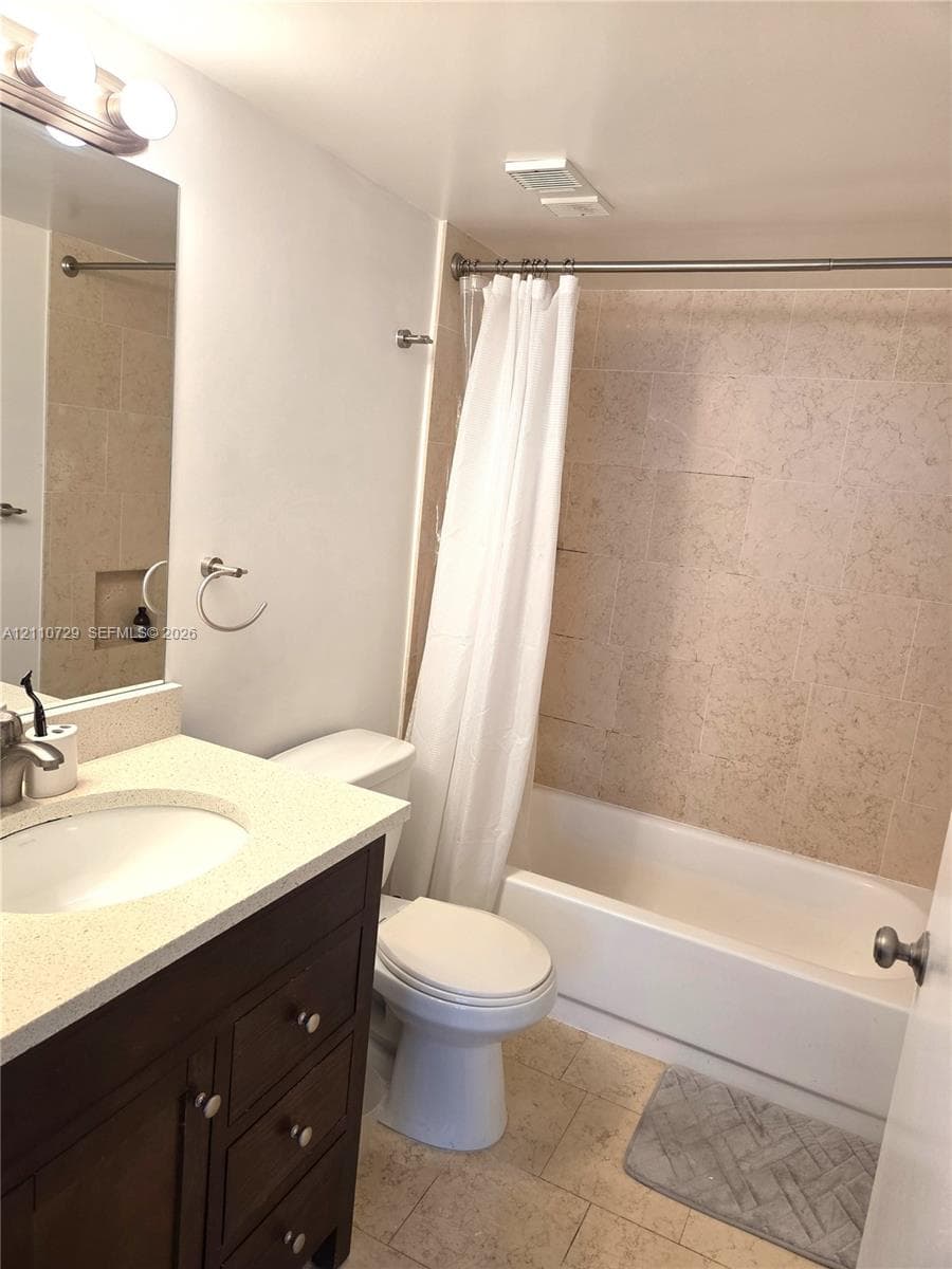 Bathroom featuring a dark wood-finish vanity with a light-toned solid surface countertop, an integrated oval basin, stone-tiled shower surround with a built-in niche, and neutral floor tiling