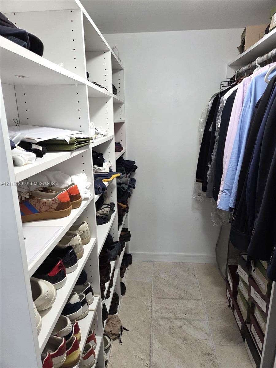 Walk-in closet featuring white built-in shelving with adjustable cubbies and integrated hanging rods, complemented by tile flooring
