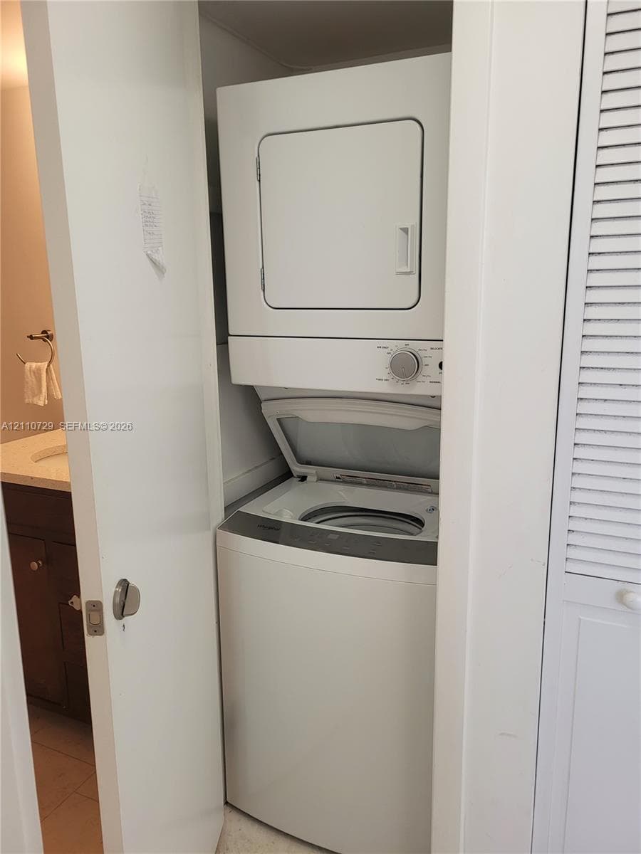 Stacked laundry unit with top-loading washer and front-loading dryer, situated within a closet enclosure featuring a louvered door