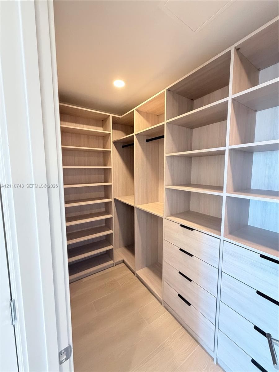 Custom walk-in closet featuring light-toned wood-finish cabinetry, floor-to-ceiling shelving, recessed lighting, and integrated drawers with matte black hardware