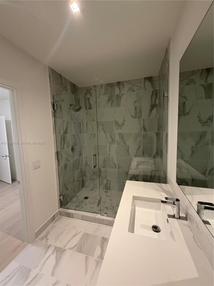 Walk-in shower with floor-to-ceiling tile, frameless glass enclosure, and wall-mounted shower head, paired with a white countertop vanity featuring an integrated rectangular sink and chrome hardware