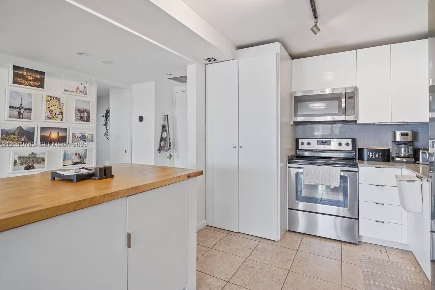 Kitchen featuring white flat-panel cabinetry, stainless steel appliances, a butcher block-topped island, and tile flooring