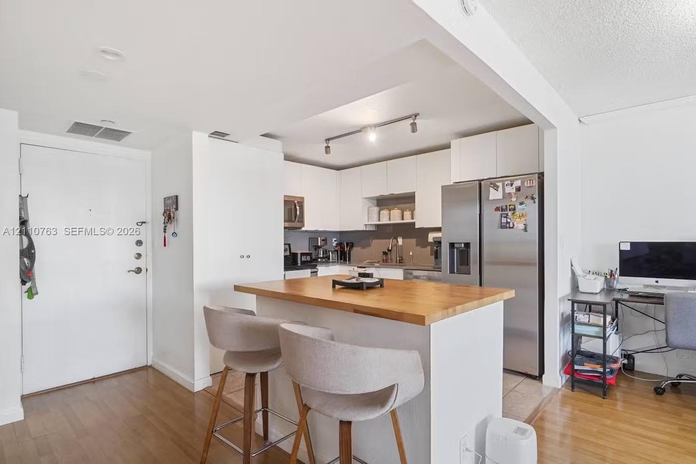 Kitchen featuring white cabinetry, wood-finish flooring, a central island with a wood countertop, stainless steel refrigerator, and recessed track lighting