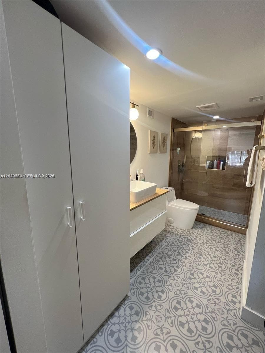 Bathroom featuring a white floating vanity with a vessel sink, patterned tile flooring, built-in floor-to-ceiling cabinetry, and a walk-in shower with glass enclosure