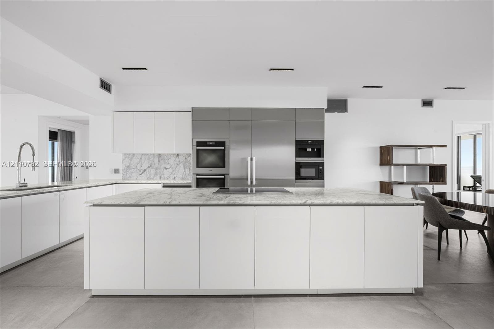 Open-concept space featuring large-format tile flooring, stainless steel integrated appliance suite, built-in shelving, and recessed ceiling lighting