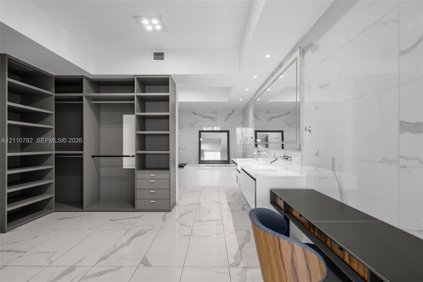 Walk-in closet featuring extensive built-in shelving, integrated hanging rods, custom cabinetry with pull-out drawers, and large-format tile flooring