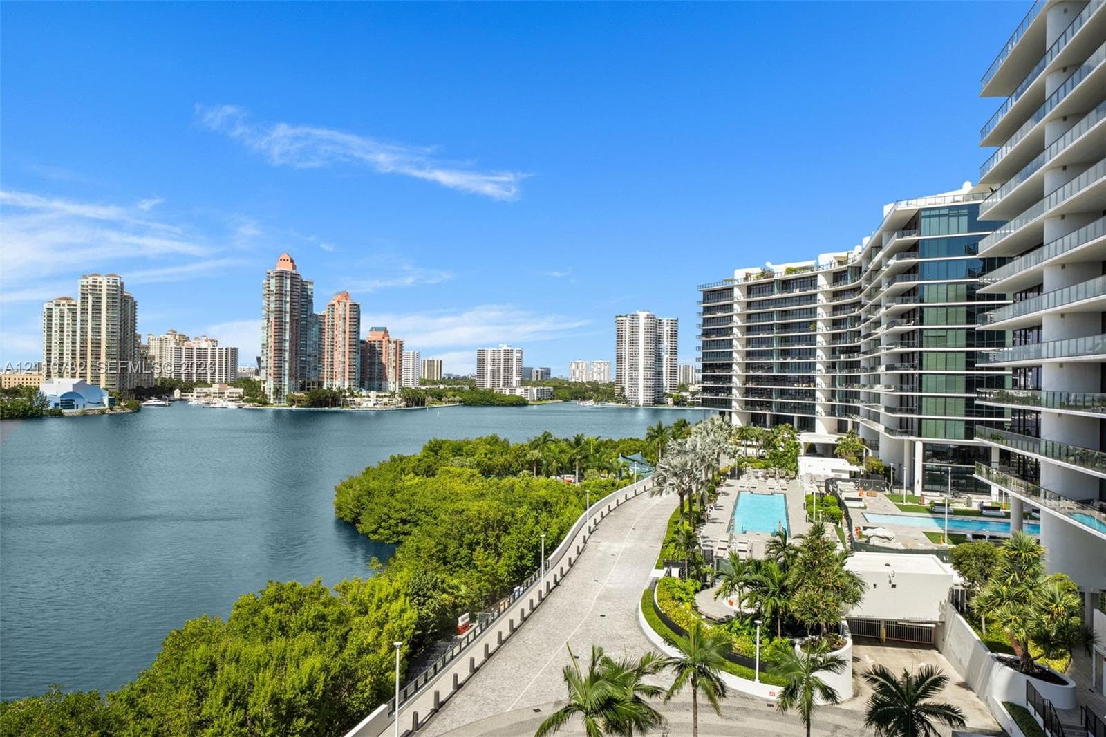 High-rise residential structure featuring tiered floor plans, expansive wrap-around balconies with glass railings, white structural pillars, and a waterfront location surrounded by mature palms