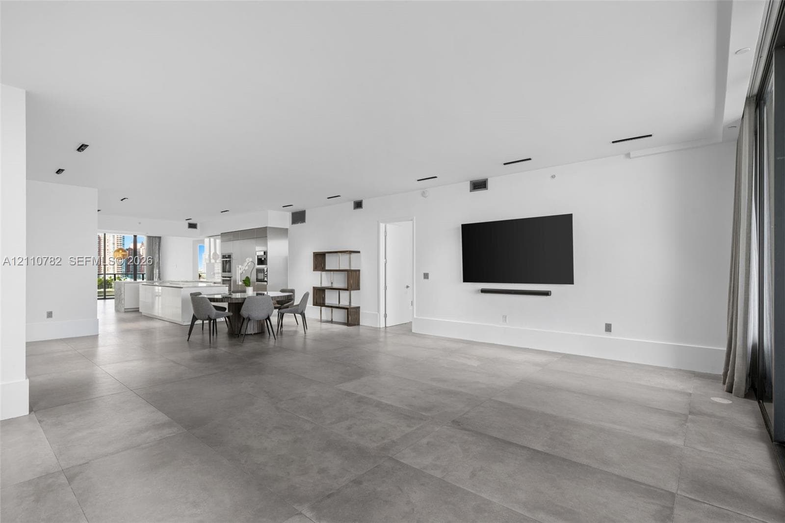 Kitchen featuring a stone-finish island with waterfall edge, white flat-panel cabinetry, stainless steel built-in appliances, and large-format floor tiling