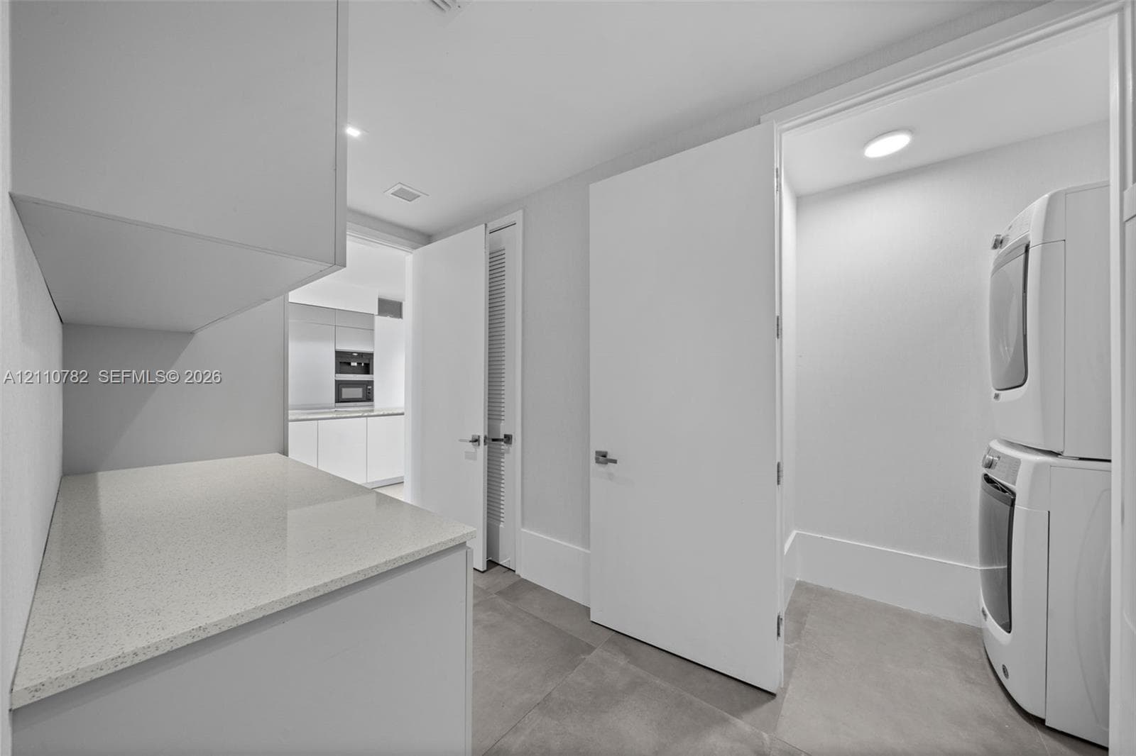Utility area featuring large-format tile flooring, built-in light-tone cabinetry, stone-composite countertops, and integrated storage shelving