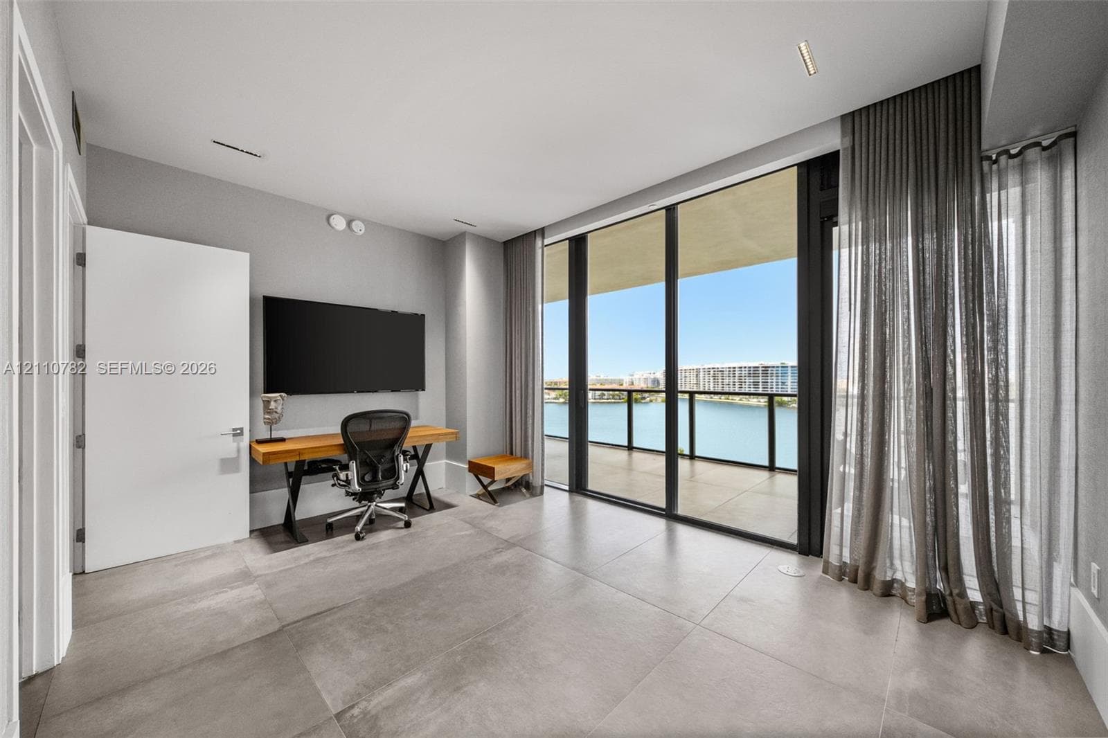 Large-format tile flooring, oversized sliding glass door, spherical glass pendant light, and balcony with water and city skyline backdrop