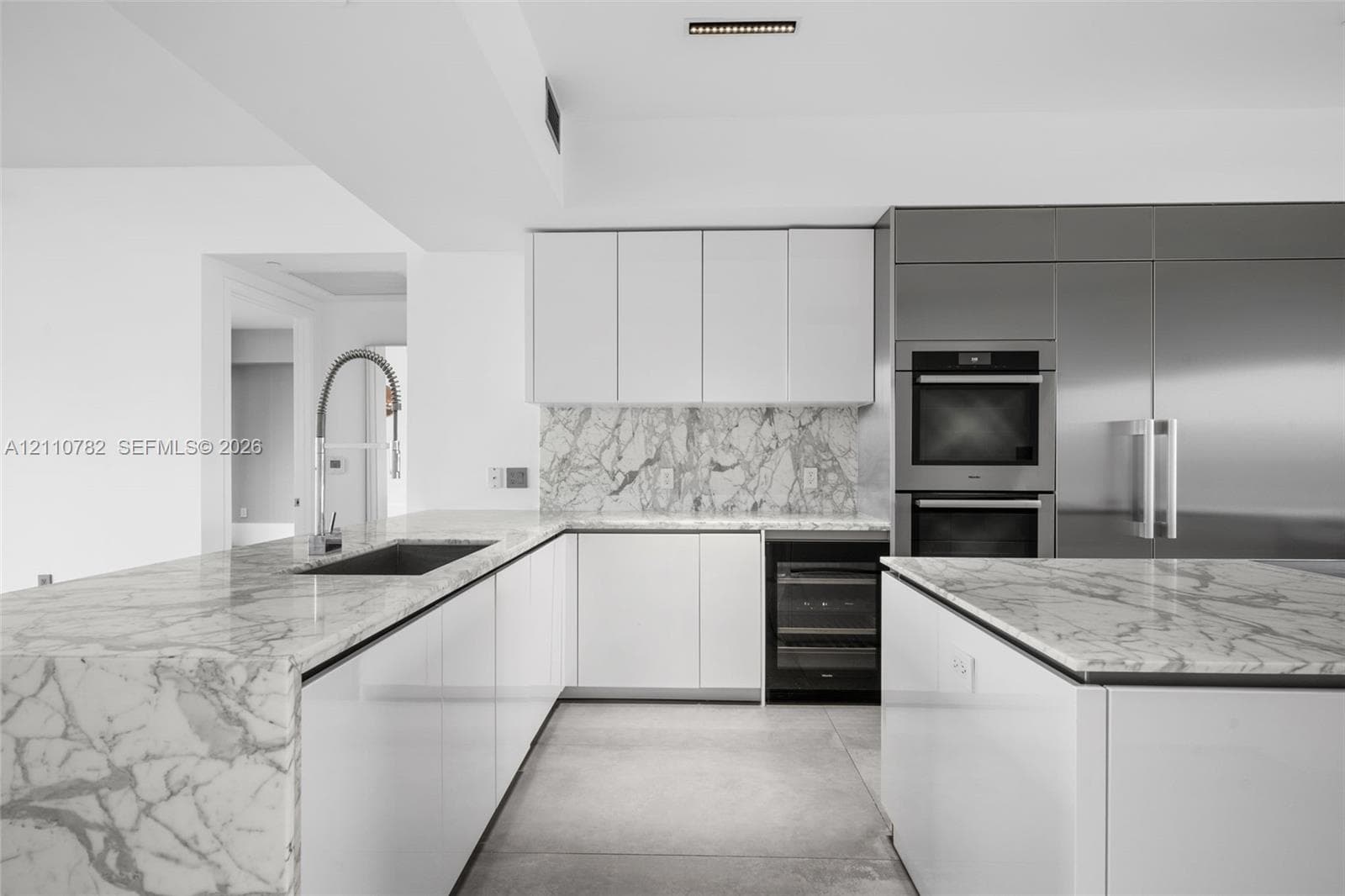 Contemporary kitchen featuring a stone-surface island with an integrated cooktop, flat-panel cabinetry, high-end built-in stainless steel appliances, and large-format floor tiling