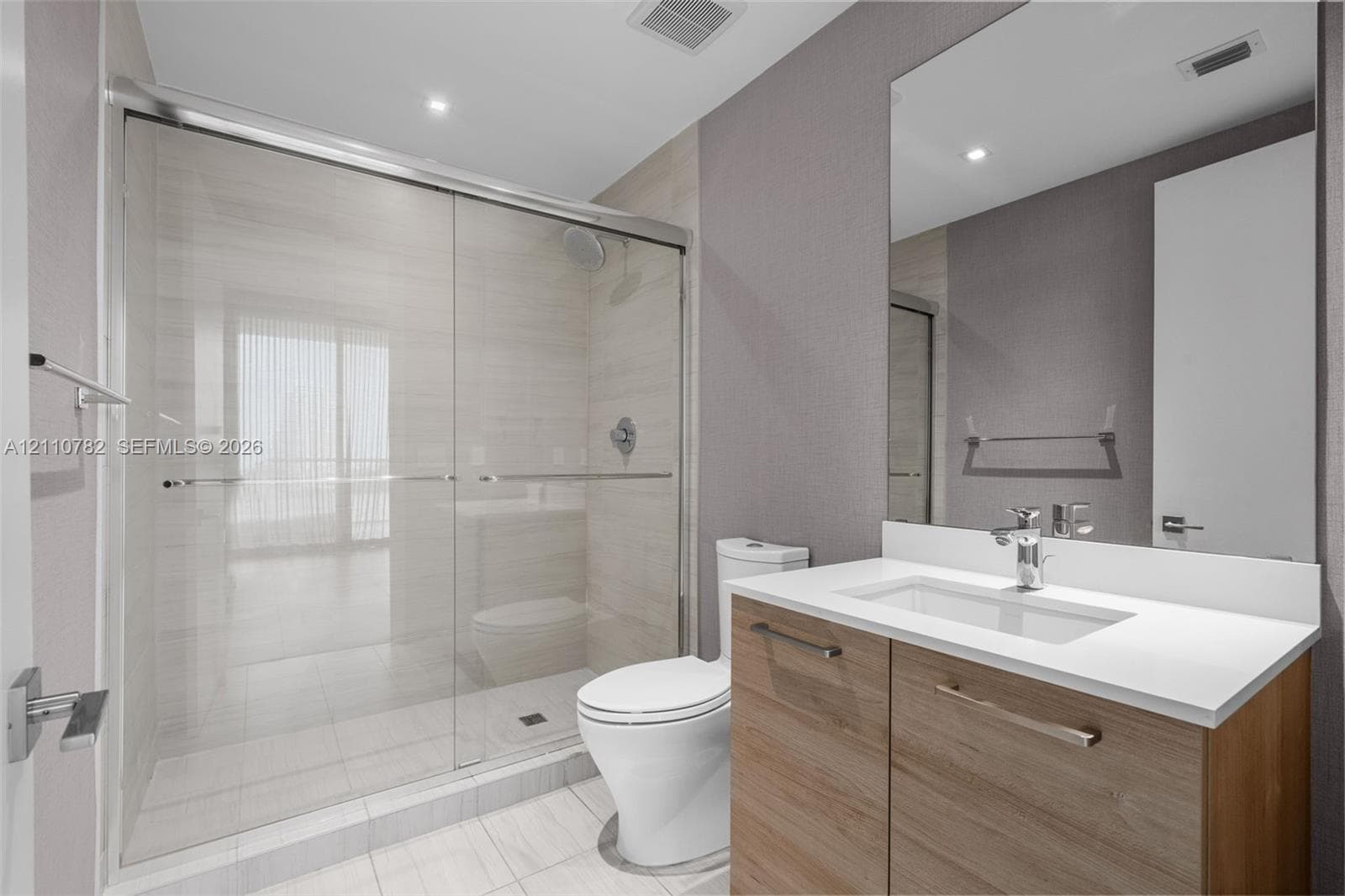 Large-format tile flooring, recessed ceiling lighting, and a walk-in closet featuring built-in shelving and integrated cabinetry