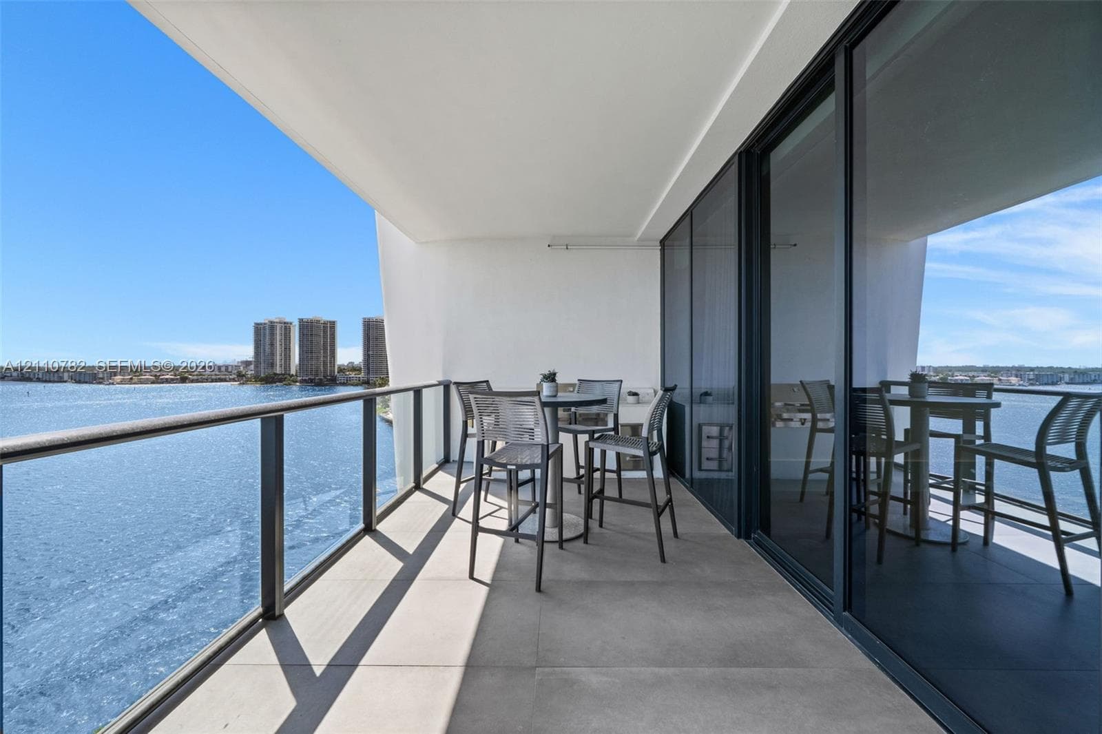 Expansive covered balcony featuring glass panel railings, tiled flooring, and floor-to-ceiling sliding glass wall panels overlooking the waterfront