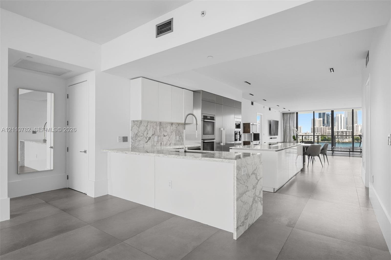 Contemporary kitchen featuring dual islands with stone-surface countertops, floor-to-ceiling cabinetry, integrated stainless steel appliances, and large-format porcelain tile flooring