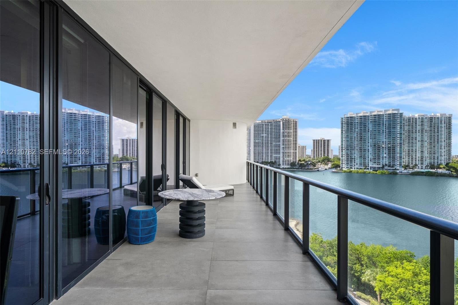 Expansive covered terrace featuring floor-to-ceiling glass panel doors, concrete-finish flooring, and a sleek glass-paneled railing with black framing