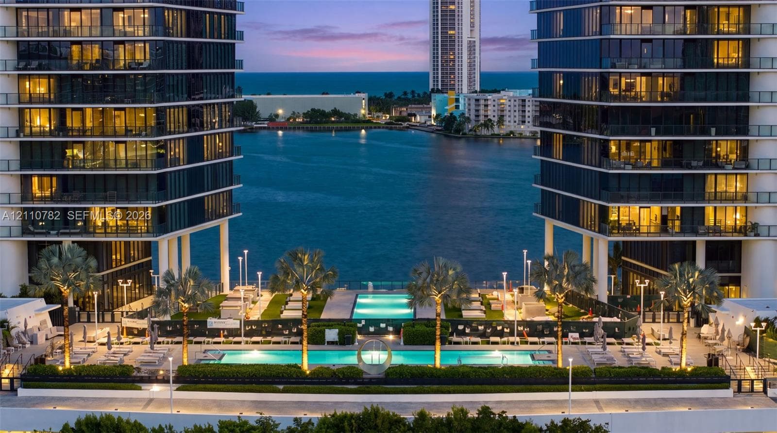 High-rise architecture with expansive glass-railed balconies, waterfront location, multi-level swimming pools, and landscaped grounds with mature palms