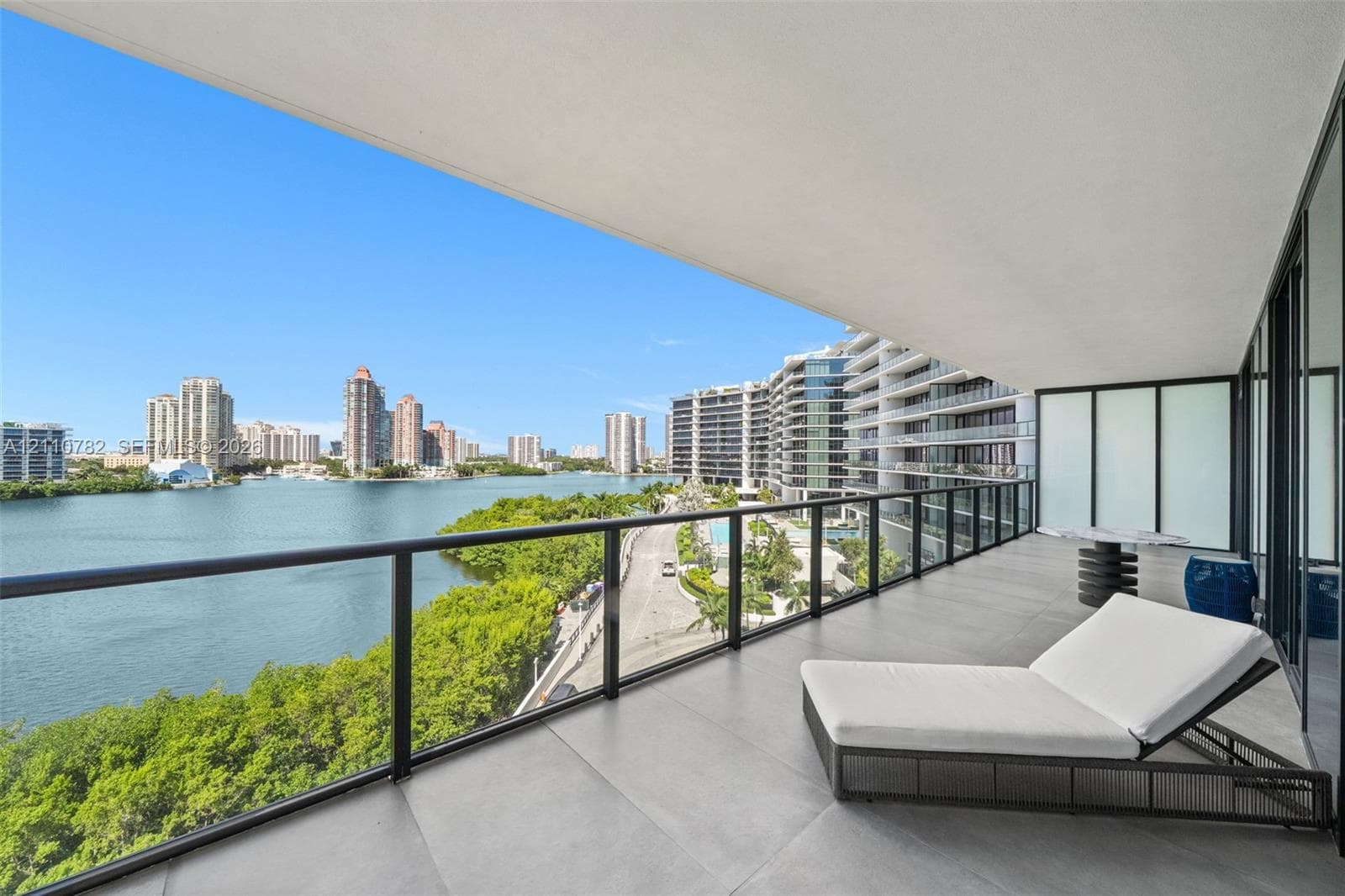 Covered balcony featuring large-format stone-finish tiling, full-height glass sliding doors, and a sleek metal railing with glass panels