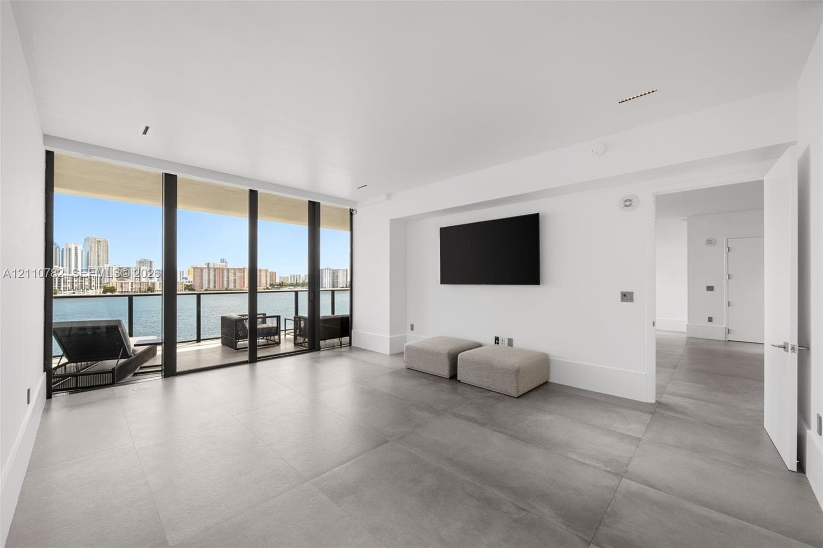 Large-format tile flooring, floor-to-ceiling glass paneling, and an attached balcony with metal railing overlooking the waterfront and cityscape