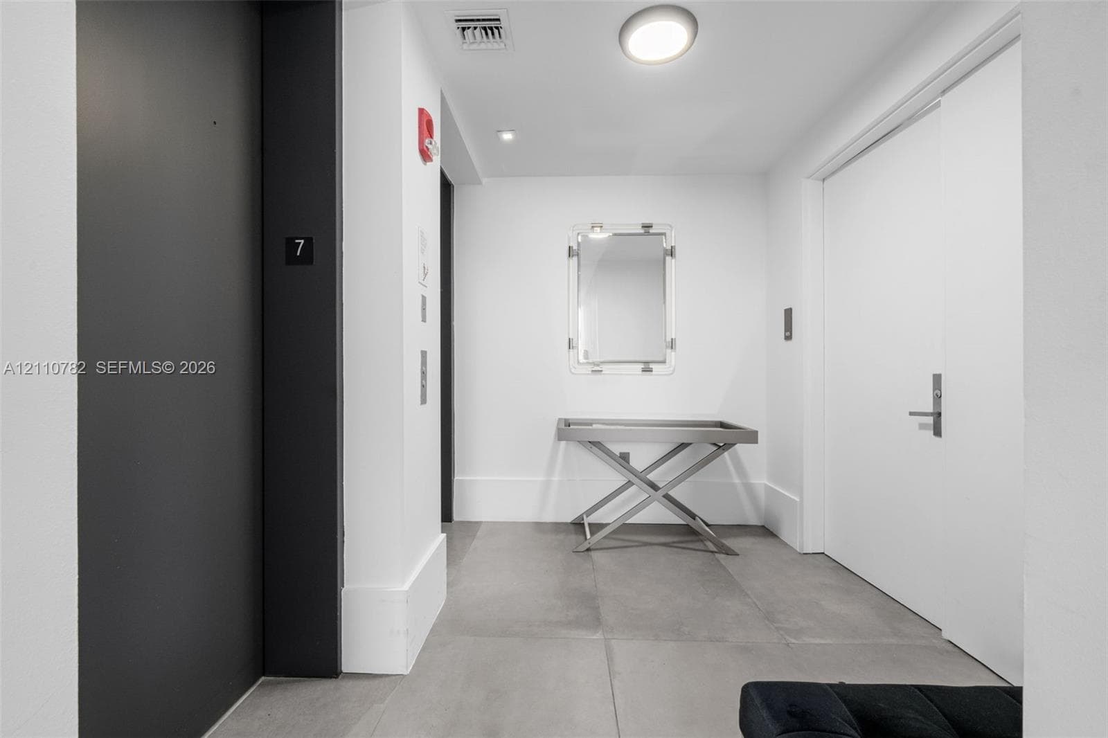 Floor-to-ceiling sliding glass doors, large-format grey tile flooring, recessed ceiling lighting, and a private balcony featuring a glass railing