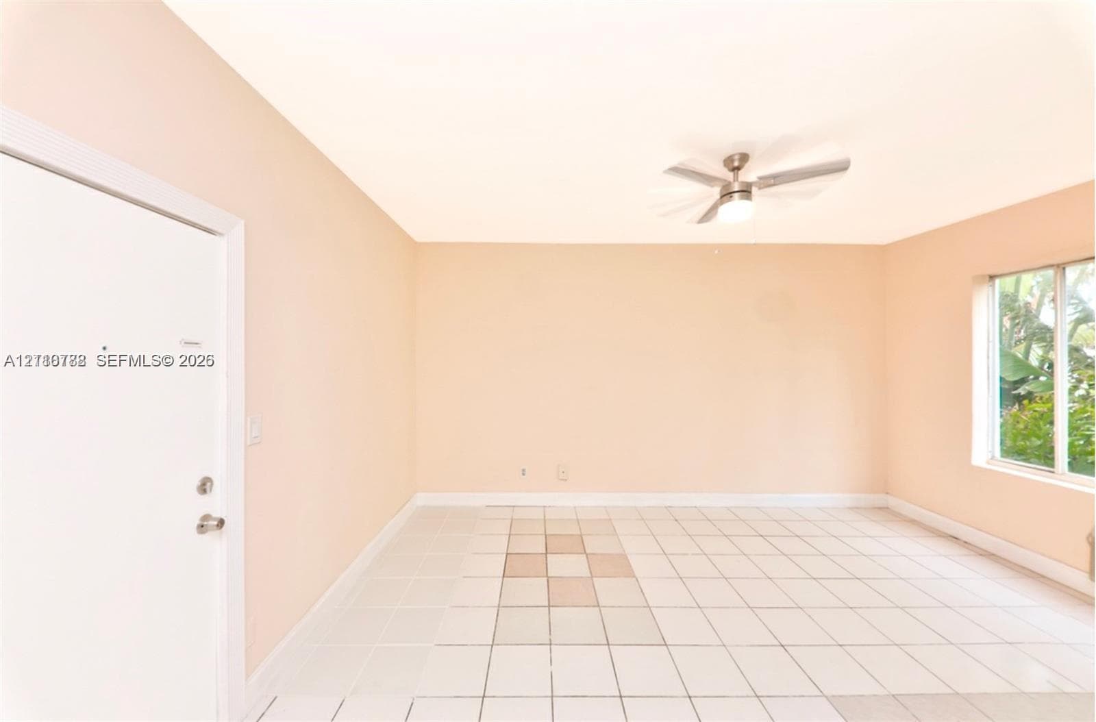 Neutral interior room featuring white tile flooring, a multi-blade ceiling fan with integrated lighting, and a single-pane window