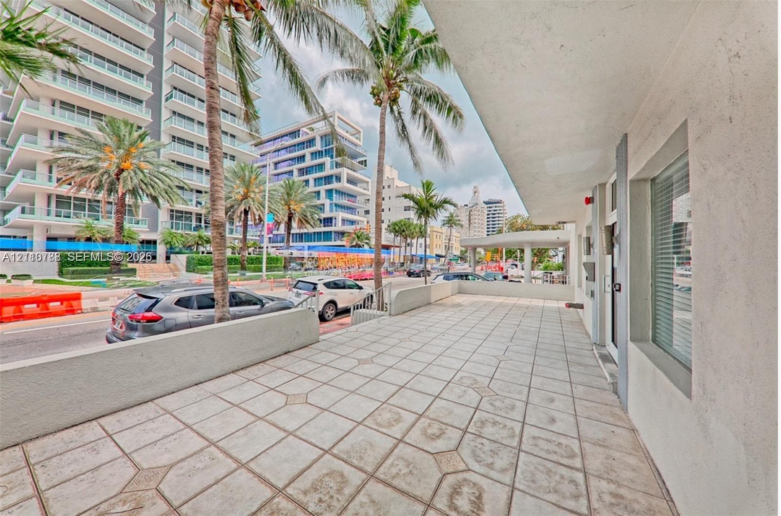Covered exterior terrace featuring geometric tile flooring, concrete perimeter wall, and built-in glass paneled entry