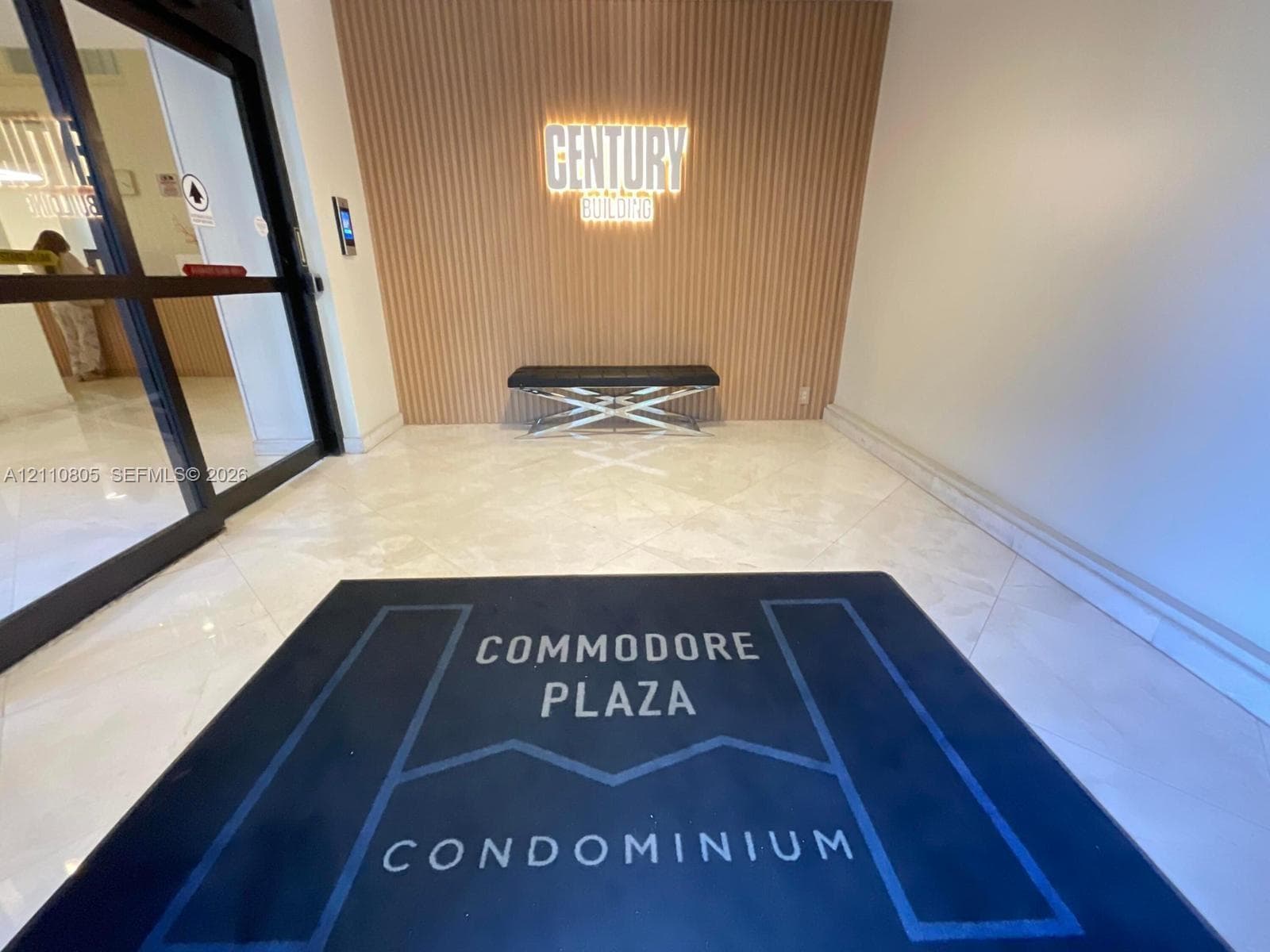Building entrance lobby featuring polished stone flooring, vertical slat wood-finish wall paneling, and illuminated signage