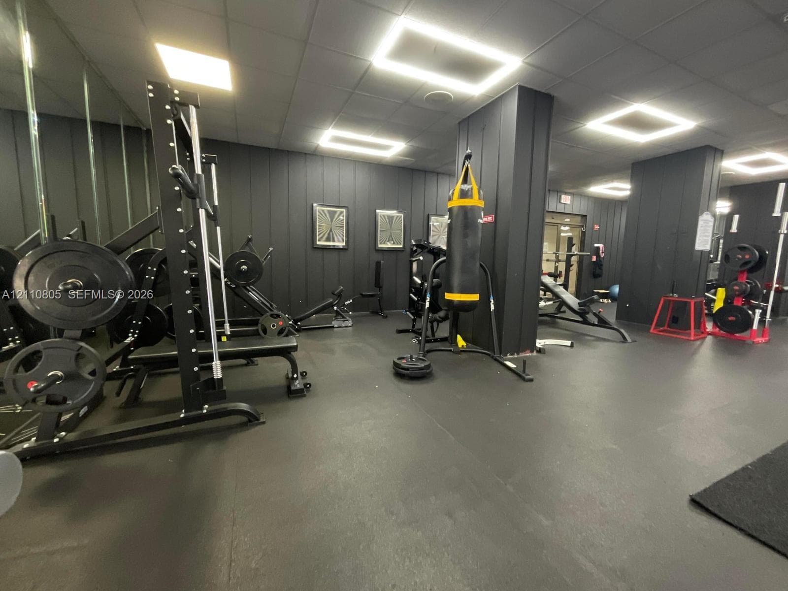 Fitness space featuring matte black vertical paneling, recessed square LED lighting, floor-to-ceiling mirrored walls, and durable rubberized flooring