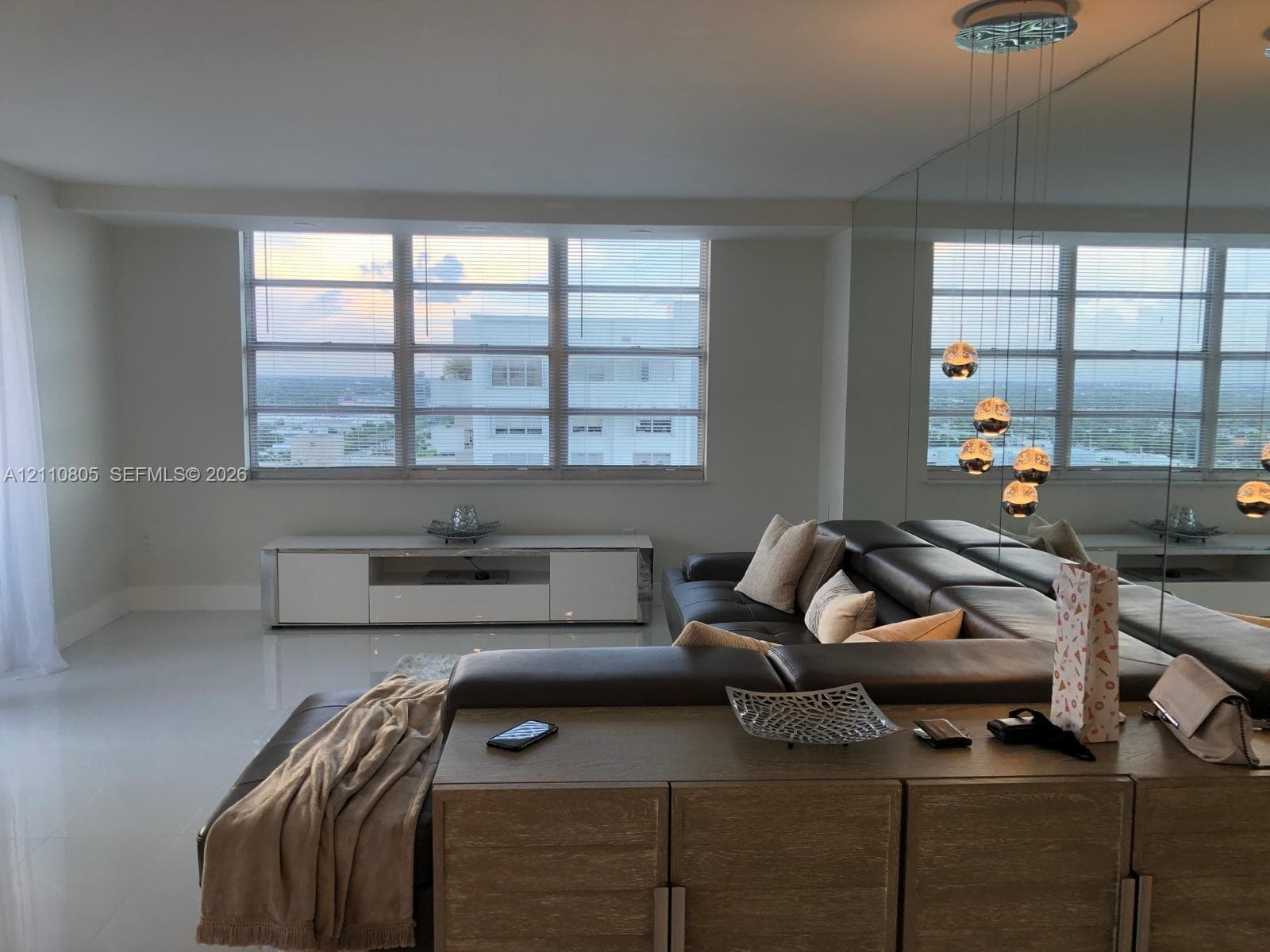 Expansive living area featuring polished tile flooring, floor-to-ceiling mirrored wall paneling, large multi-pane windows, and contemporary multi-pendant lighting