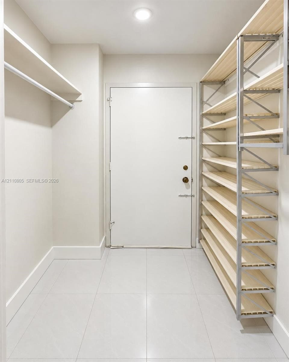 Storage space featuring floor-to-ceiling multi-tiered wooden shelving, white tile flooring, recessed ceiling lighting, and a neutral color palette